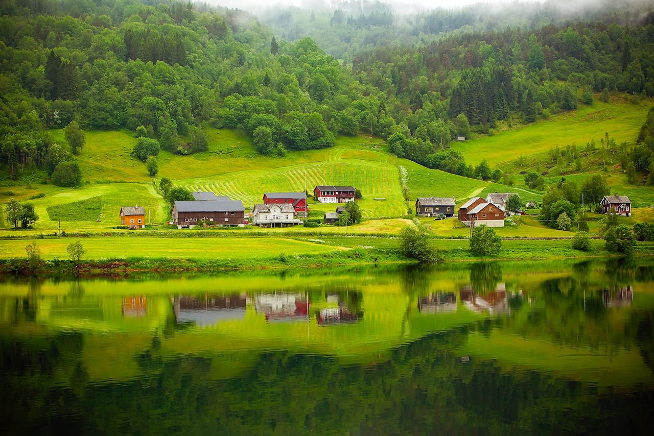 Tranquil countryside scene with houses reflected in a calm river.